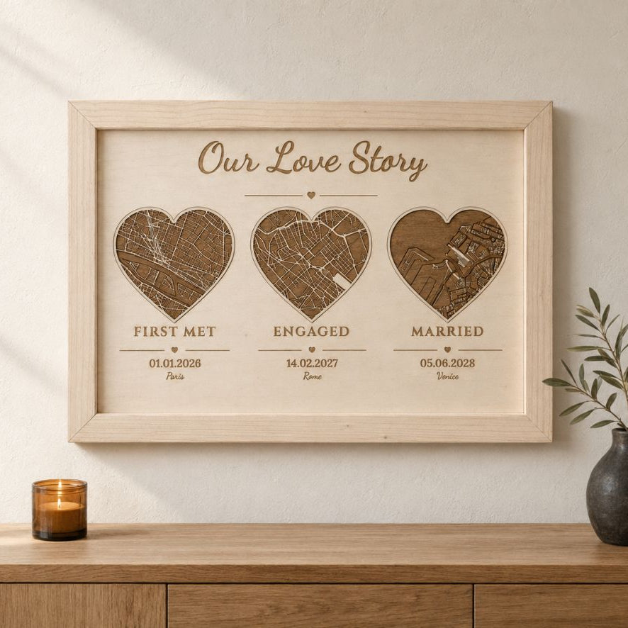 A framed personalized wooden map print titled 'Our Love Story' hangs on a light wall above a wooden console table. The artwork shows three heart-shaped map cutouts labeled First Met, Engaged, and Married with dates beneath them.