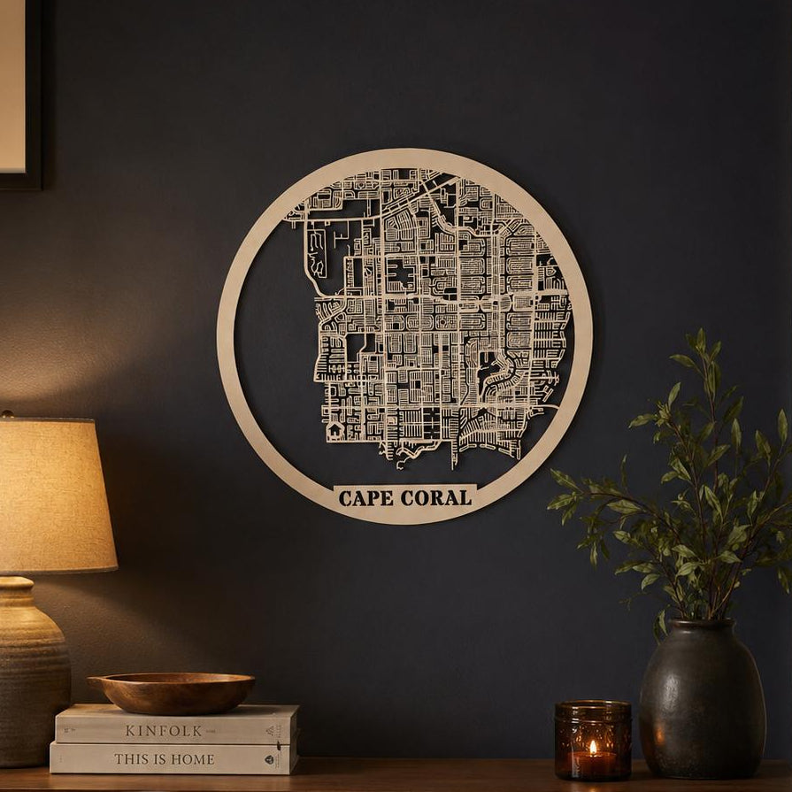 A circular wooden map wall art piece featuring Cape Coral, displayed on a dark navy wall above a wooden console table in a styled living room setting.