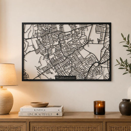 A framed black-and-white map wall art piece labeled 'Walthamstow' hangs on a beige wall above a wooden console table styled with a lamp, books, candles, and a vase with greenery.